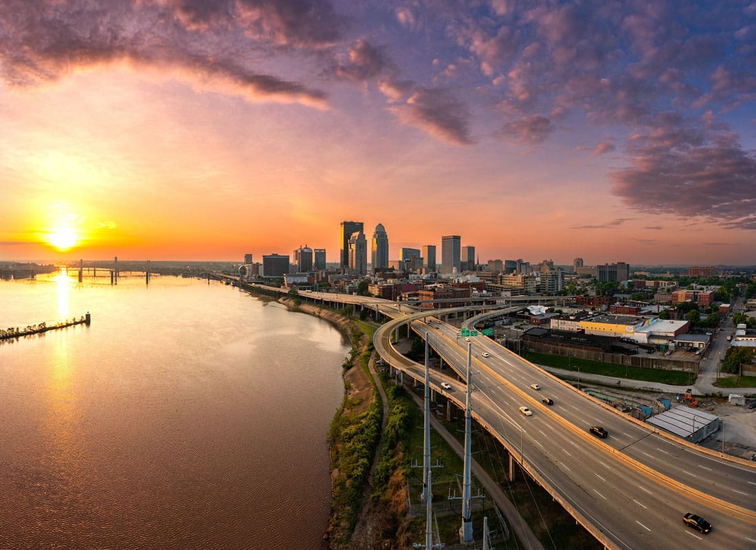 Louisville, KY - Aerial View of a Highway Next to the Water with Views of Building in Downtown Louisville Kentucky Against a Colorful Sky